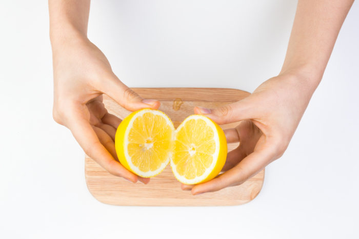 Ett par kvinnohänder håller en delad citron ovanför en träskärbräda.